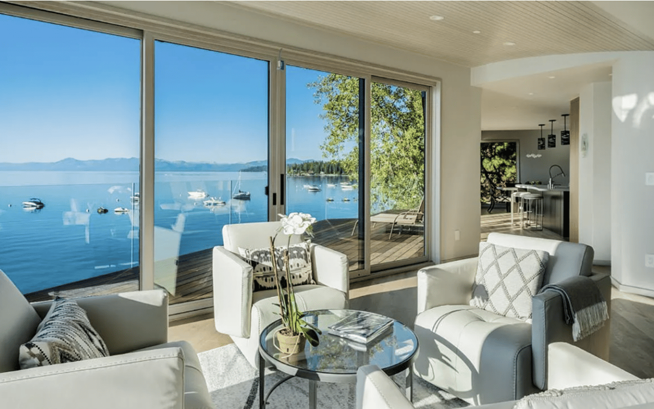 Furnished living room with expansive lake and mountain views through sliding glass doors.