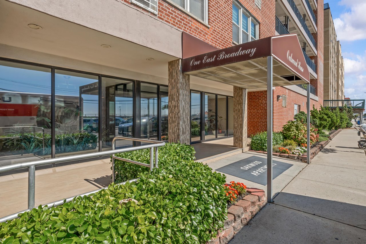 Oakwood House cooperative entrance with a brick facade, glass doors, and landscaped sidewalk.