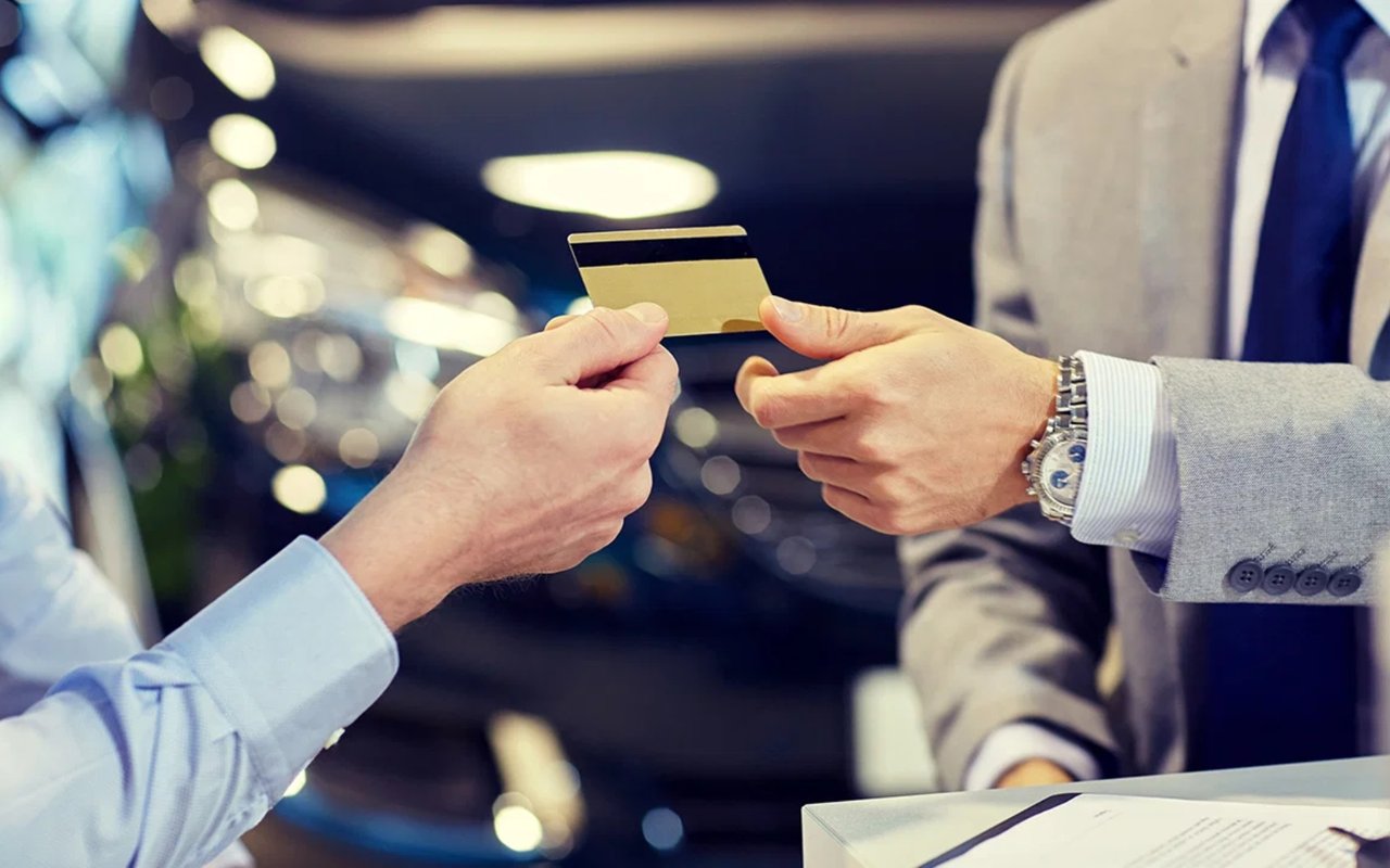 A customer hands a credit card to a salesperson in a gray suit.