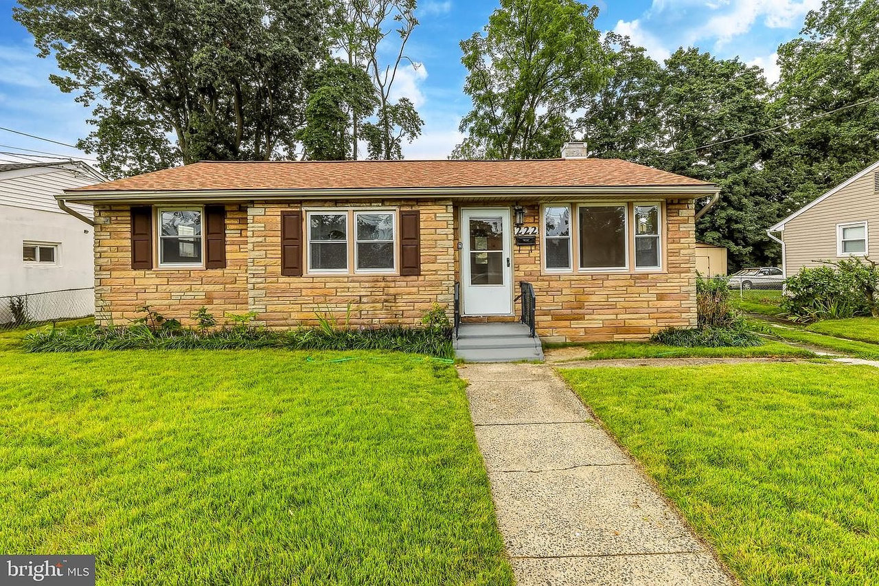 Single-story stone ranch house with brown shutters, a front walkway, and a broad green lawn.