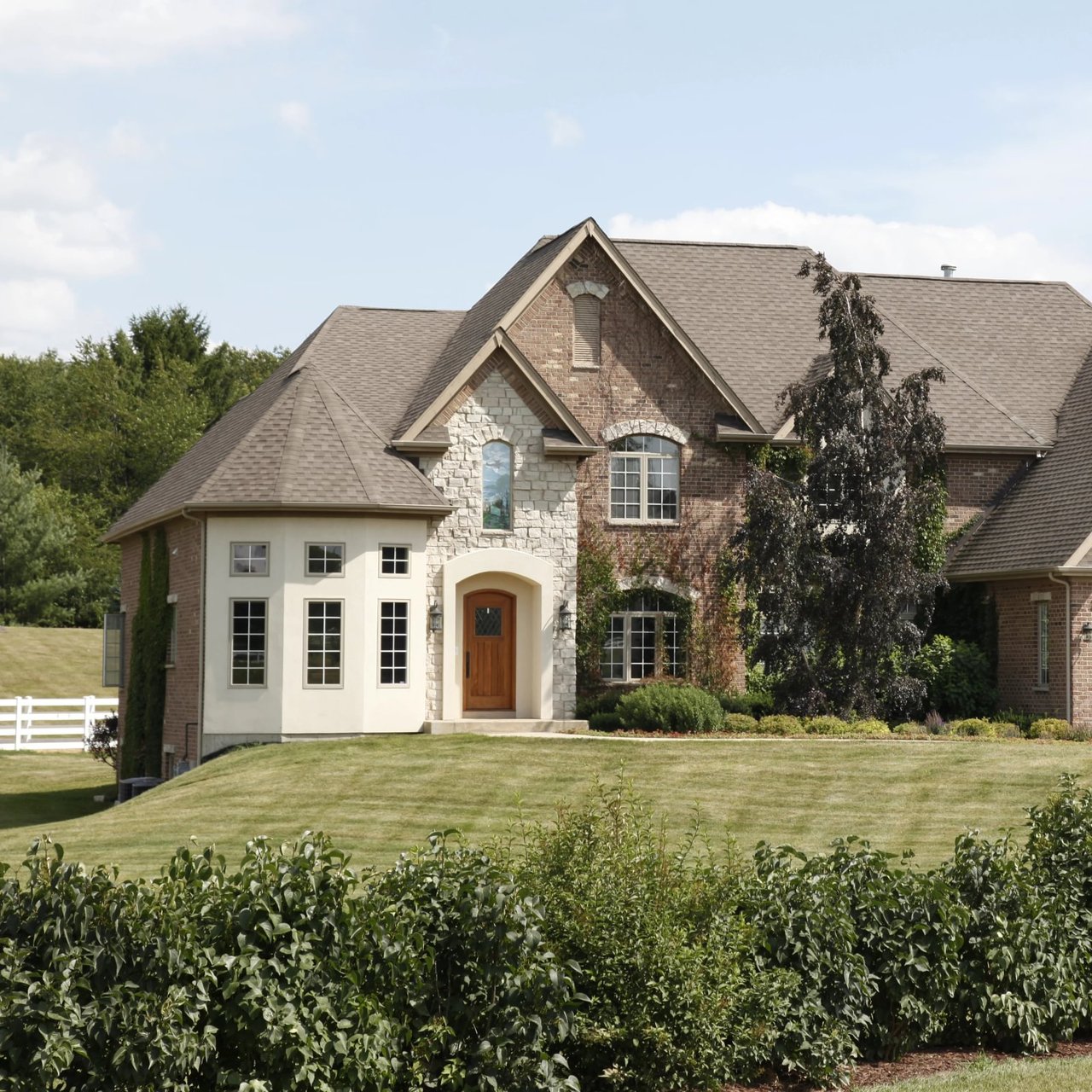Two-story brick and stone home with a gabled roof, arched wooden entry, and landscaped lawn.