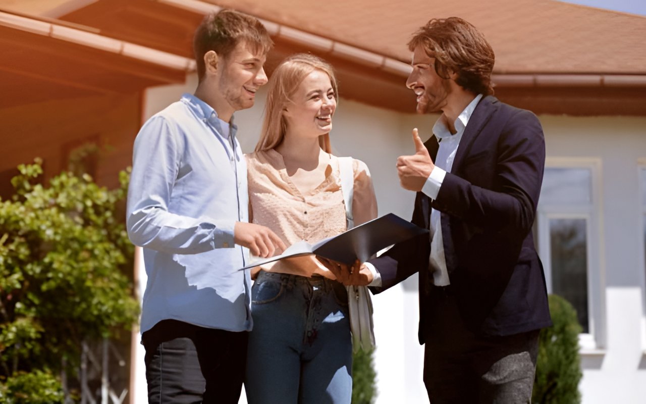 Real estate agent discusses a folder with a smiling couple outside a house.