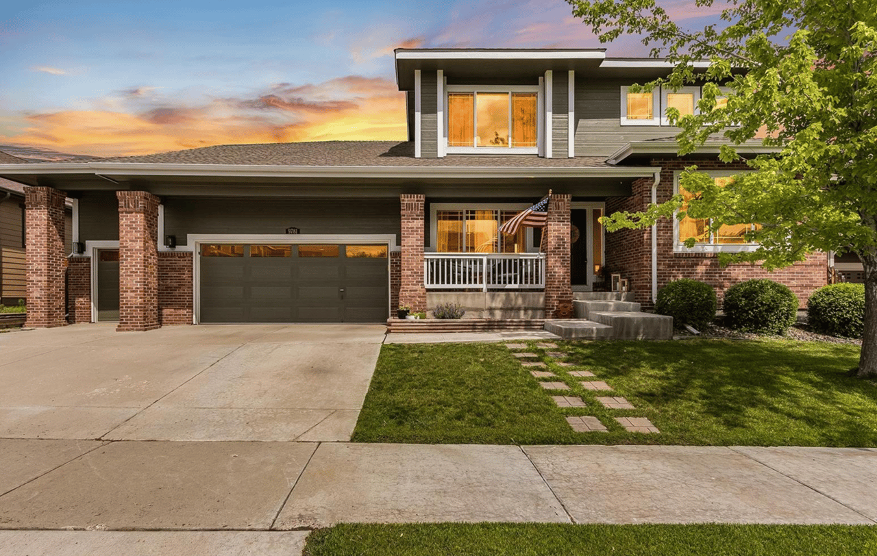 Two-story brick-and-siding home with a covered porch, American flag, and stepping-stone lawn path.