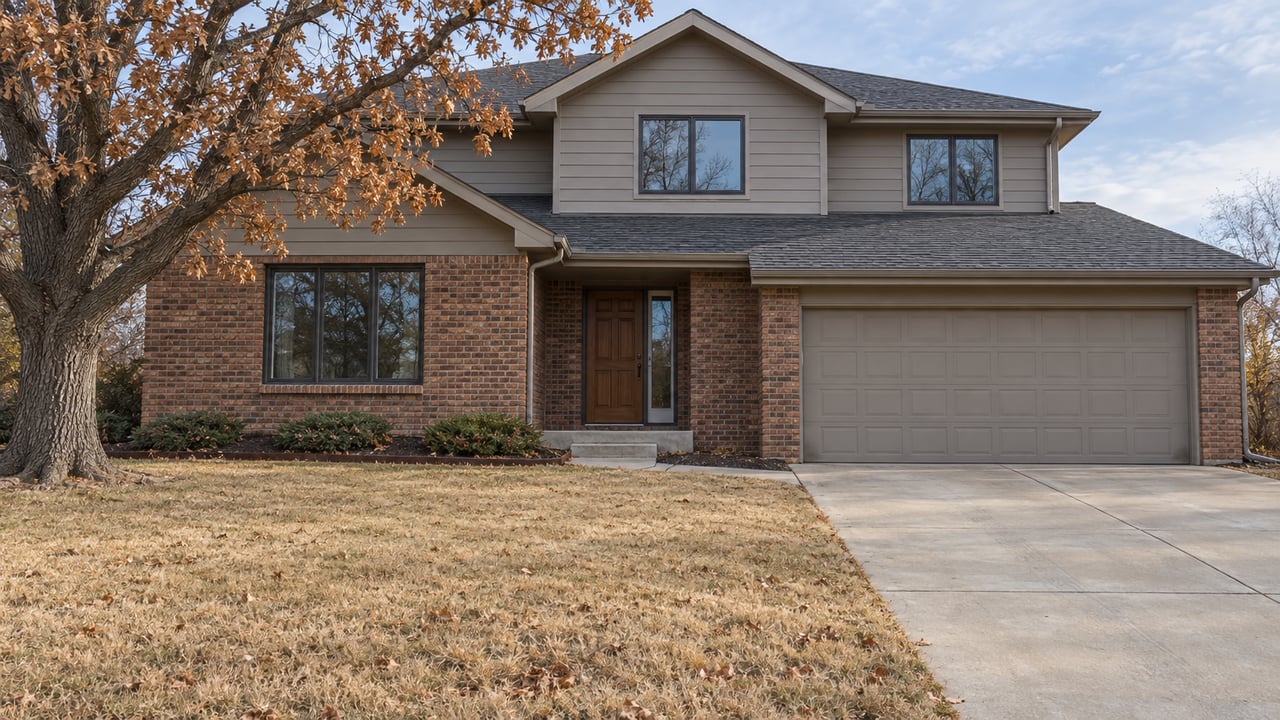 Late-autumn light on a gabled brick-and-siding home, with a deep dormant lawn, a mature bur oak and a concrete driveway.