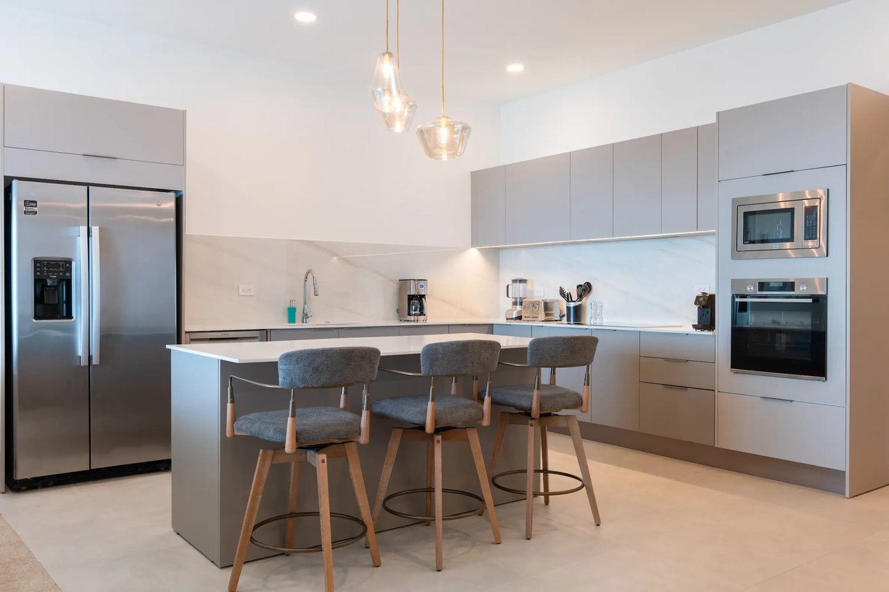 Modern condo kitchen with a large island, three bar stools, and stainless steel appliances.