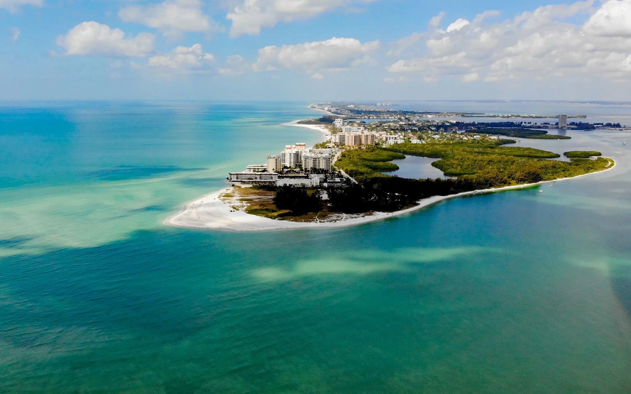 Aerial view of a Miami island with waterfront buildings, sandy beaches, and turquoise water.