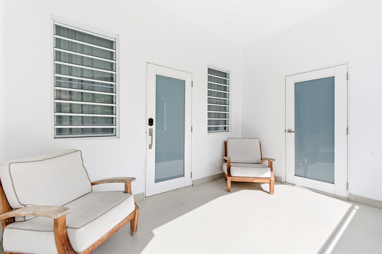 Sitting area with wood-framed chairs, frosted-glass doors, and louvered windows.