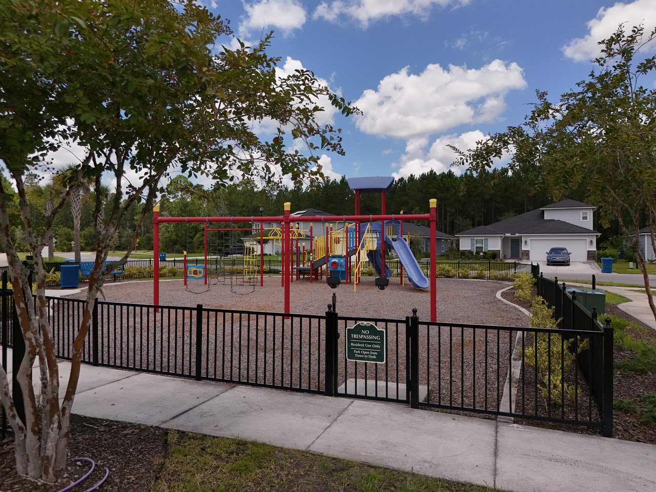 Community playground with colorful play equipment and a blue slide behind a black fence.