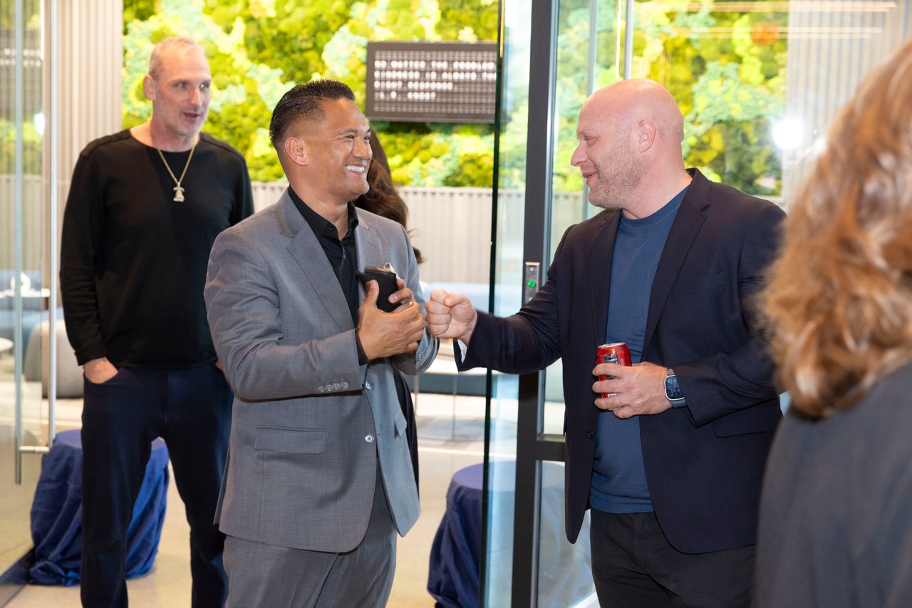 Guests mingle at an open house as two men greet each other with a fist bump.