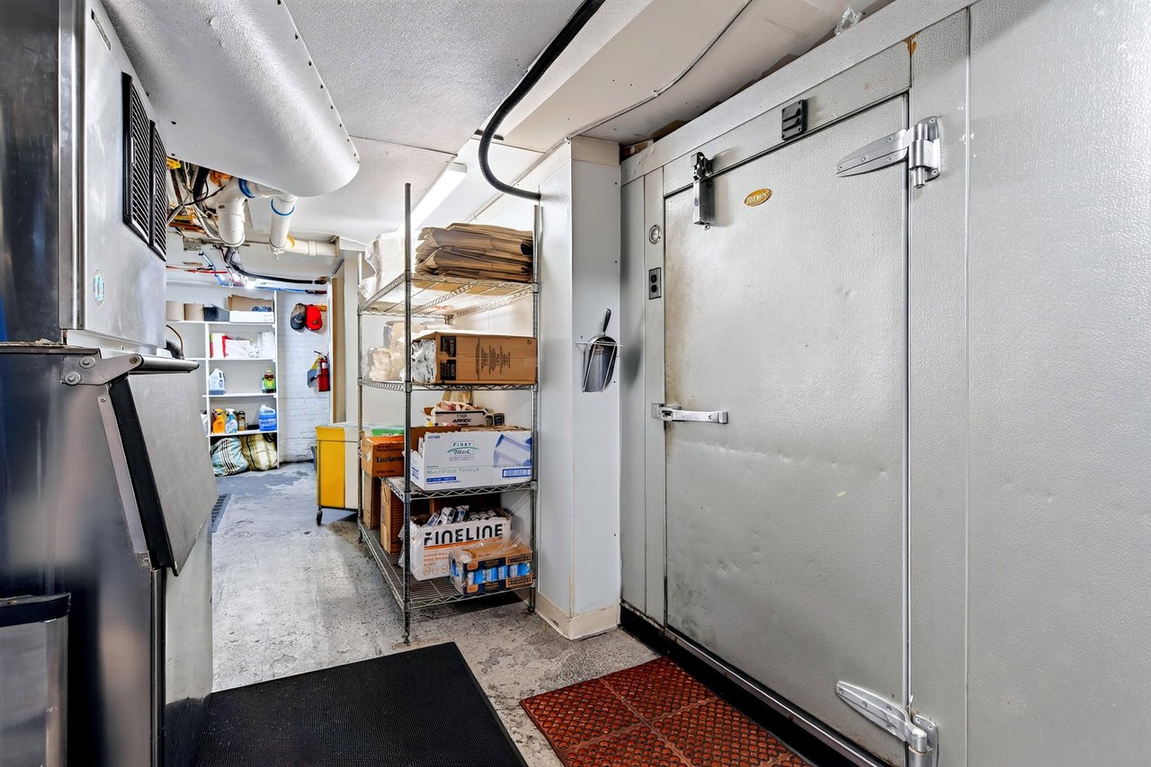 Restaurant walk-in refrigerator beside commercial equipment and supply shelves.