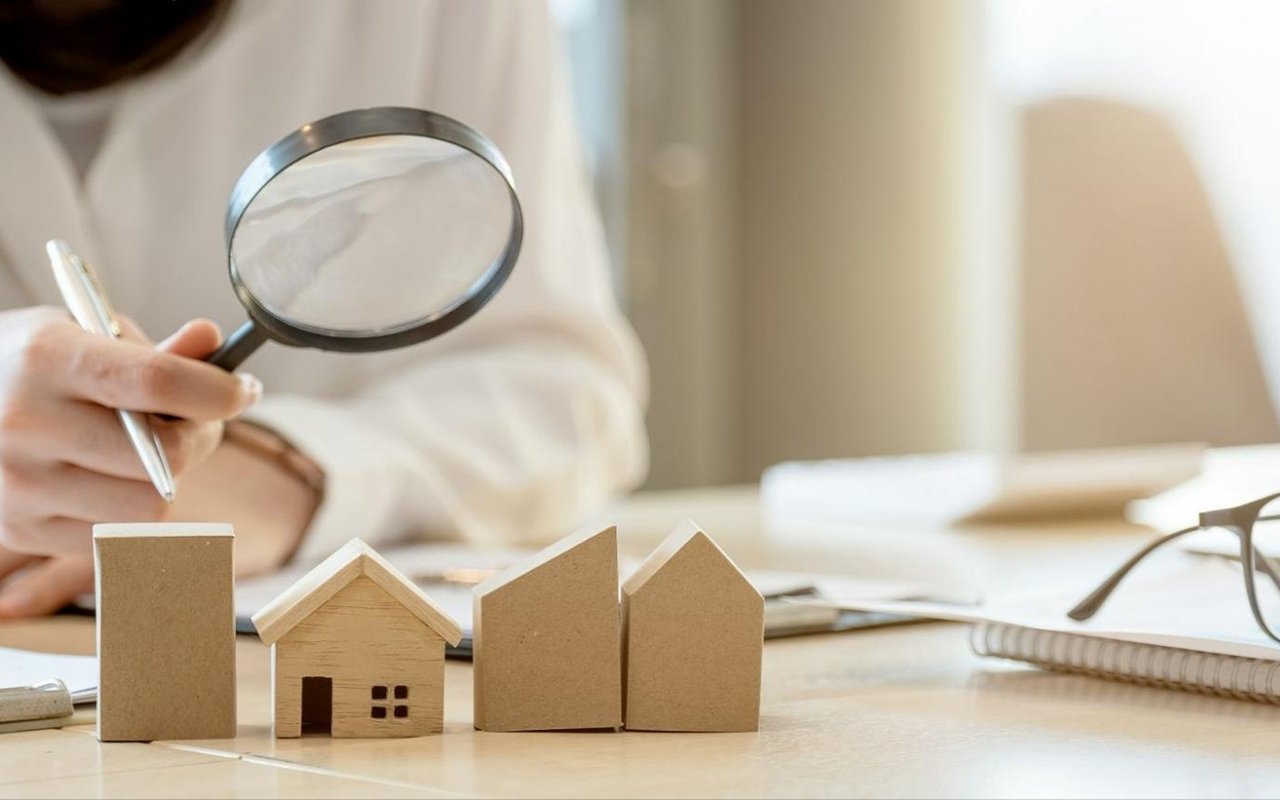 Person examines miniature model houses with a magnifying glass at a desk.