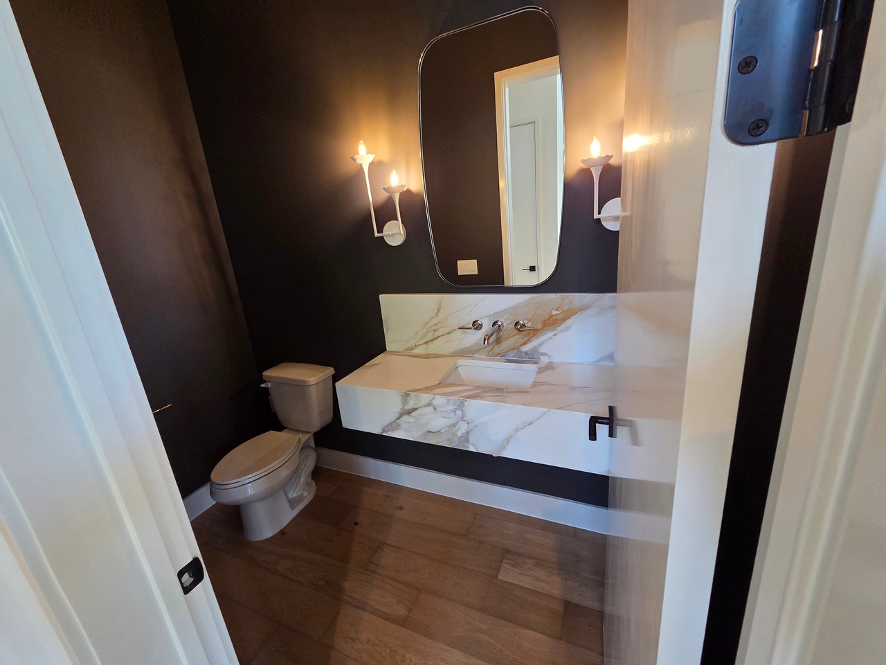 Powder room with a floating marble vanity, tall mirror, and dark walls.