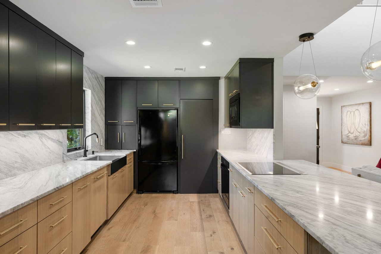 Modern kitchen with charcoal cabinets, marble counters, and a large island with cooktop.