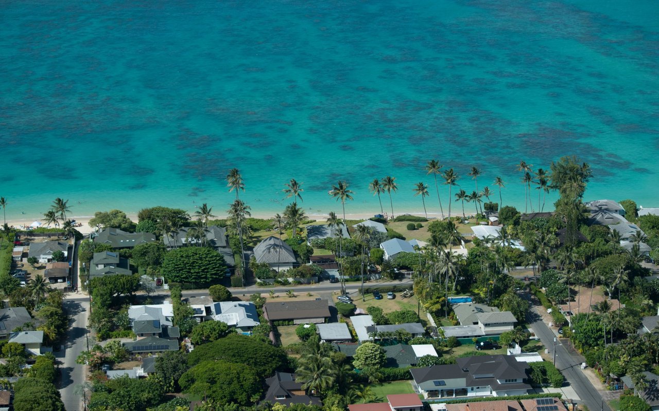 Aerial view of beachfront homes and palm trees beside turquoise water.