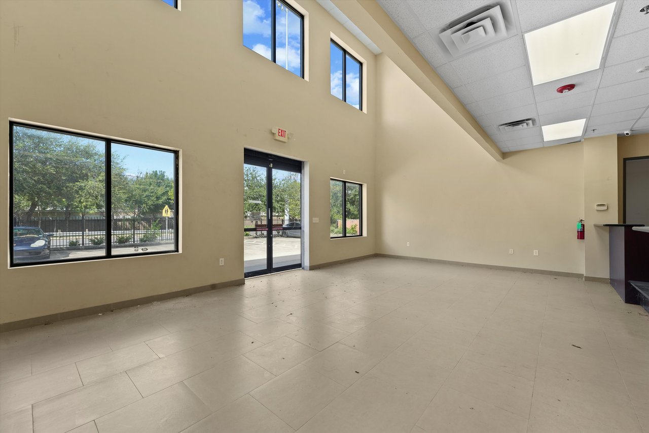 Vacant commercial interior with a tiled floor, high windows, and glass entry doors.