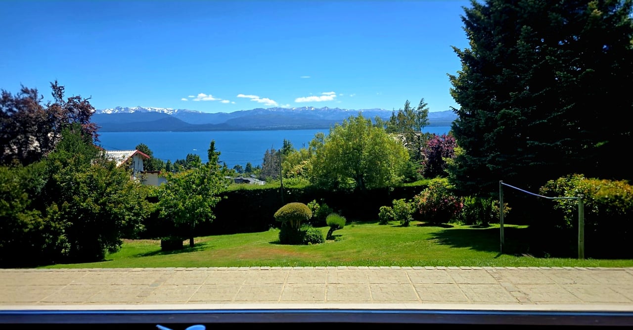 Landscaped garden overlooking a lake and snow-capped mountains, with a stone terrace in the foreground.