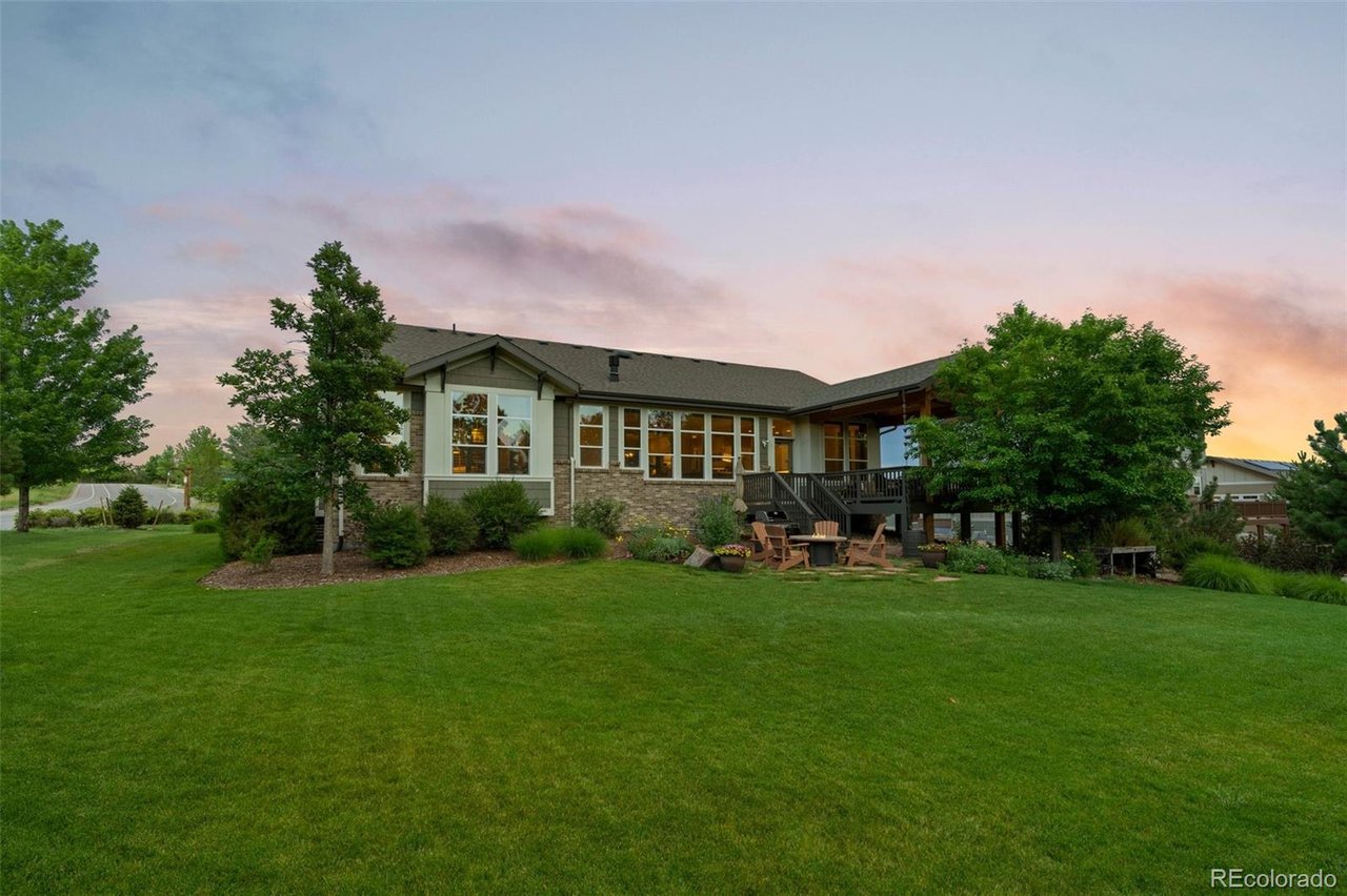 Single-story house with a raised deck and broad green lawn beneath a colorful sunset sky.