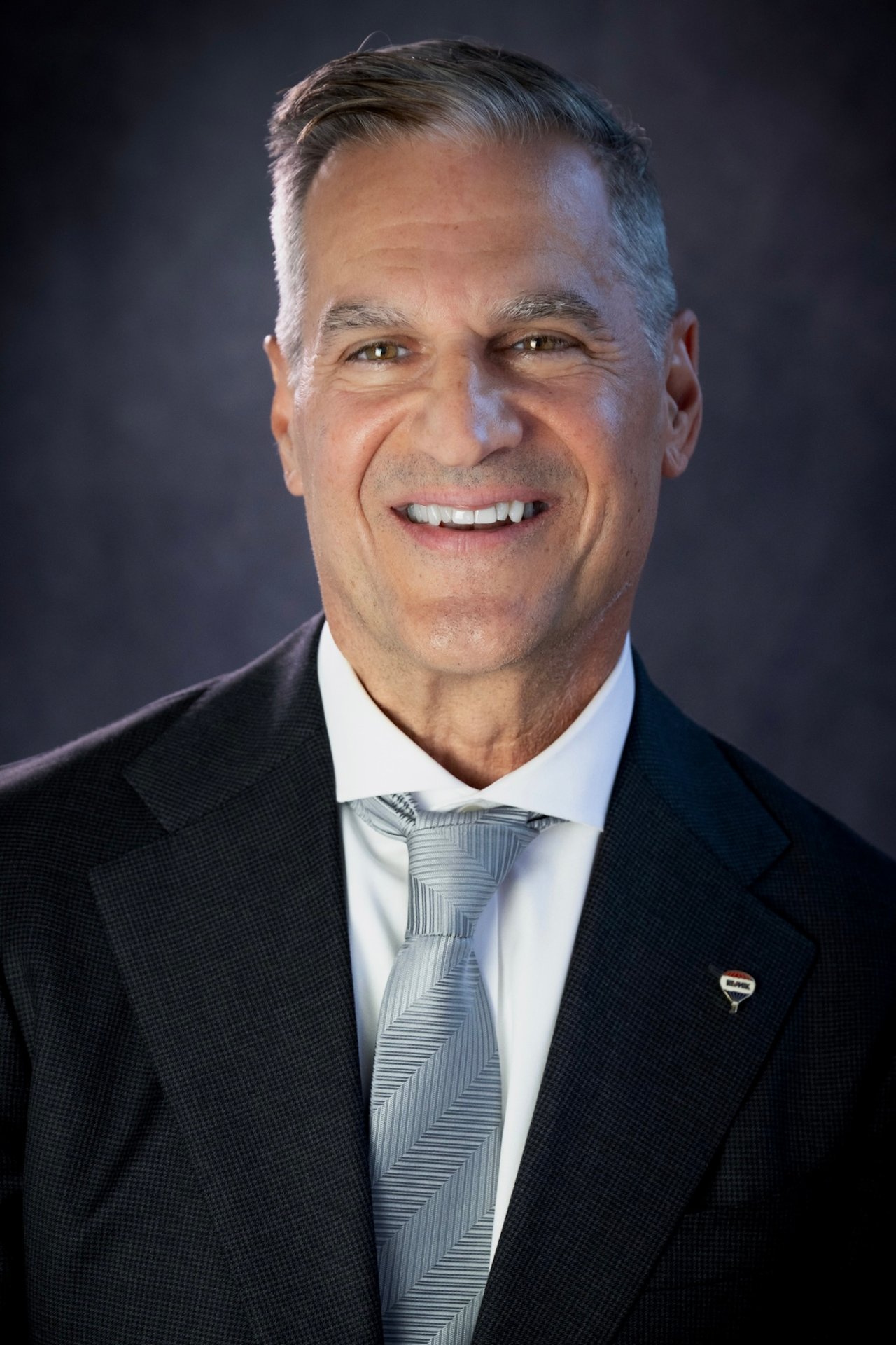 Christopher Hanna smiling in a dark suit and silver tie.