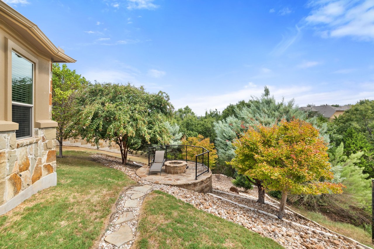 Landscaped backyard with a flagstone path, raised fire-pit patio, and mature trees.