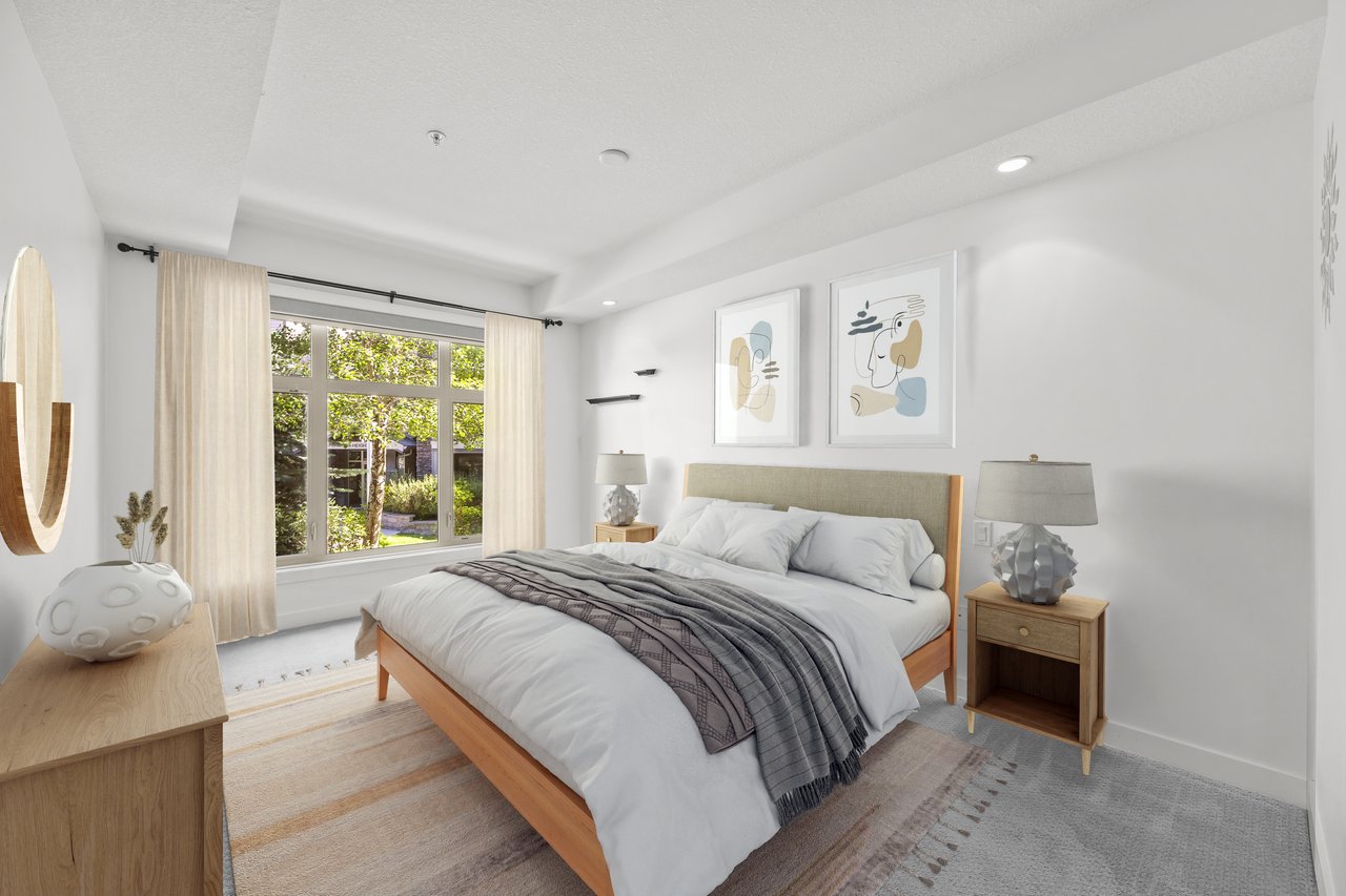 Staged bedroom with a wood-framed bed, gray throw, and large curtained windows.