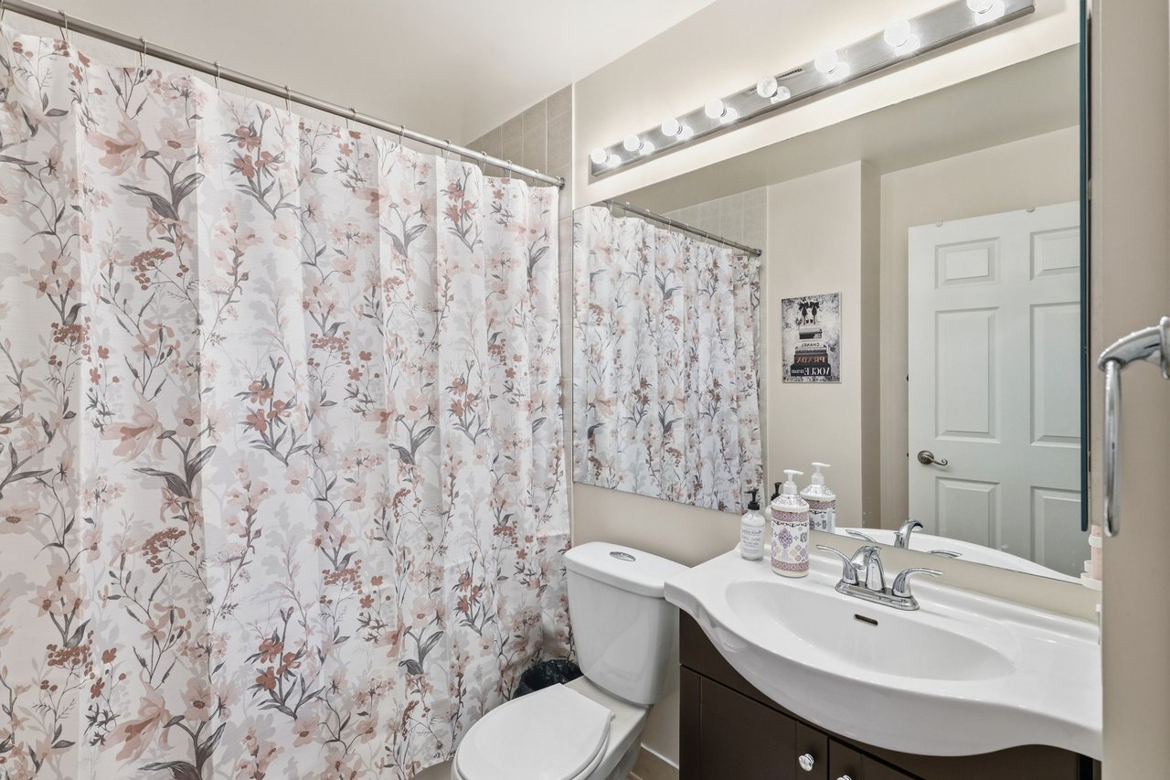 Bathroom with a floral shower curtain, white toilet, and dark vanity beneath a large mirror.