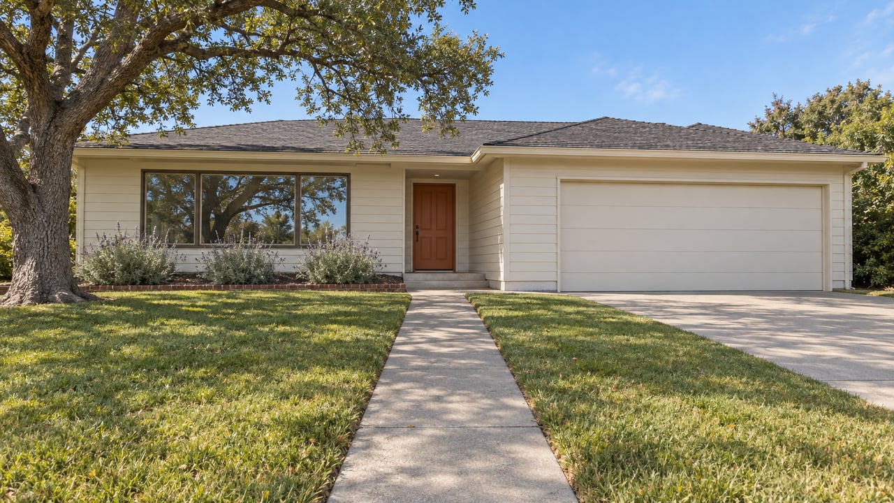 Single-story home with cream siding, an orange entry door, a deep front lawn and a mature oak in clear daylight.