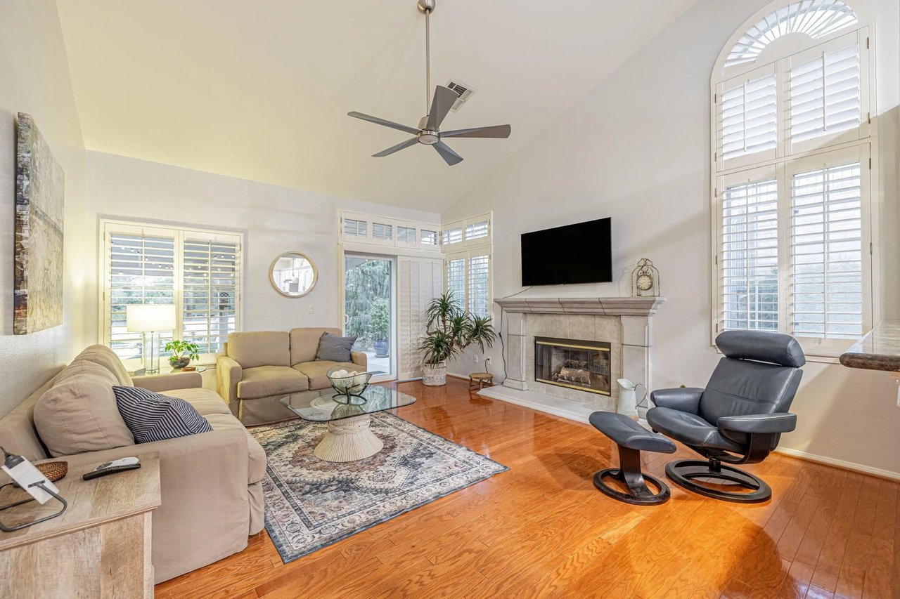 Living room with a fireplace, tall shuttered windows, beige sofas, and hardwood floors.