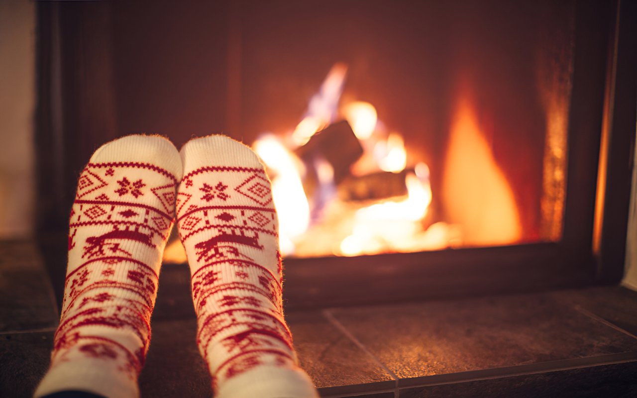 A lit fireplace behind feet in red-and-white patterned knit socks.