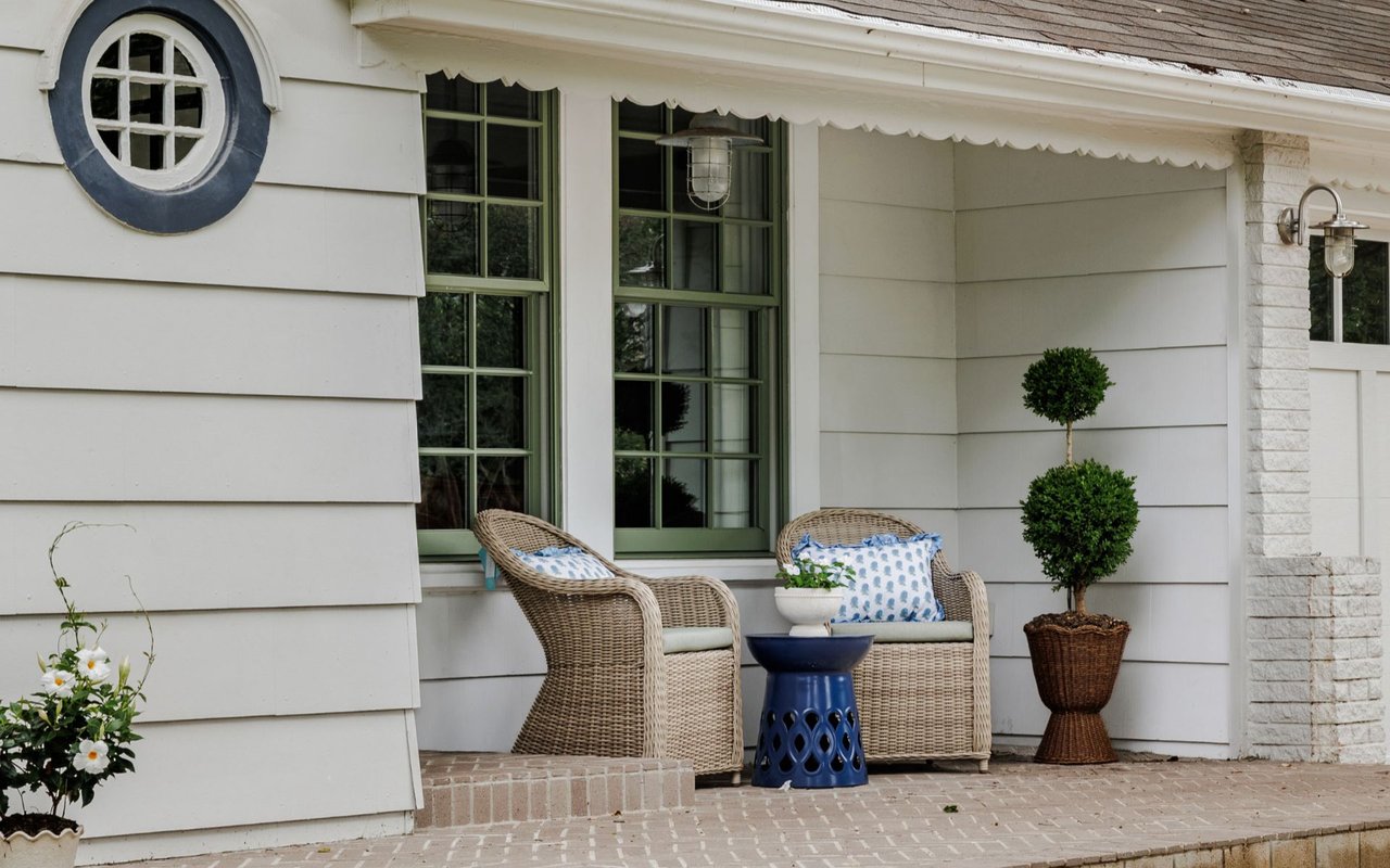 Front porch with wicker chairs, blue accents, green-trimmed windows, and a round porthole-style window.