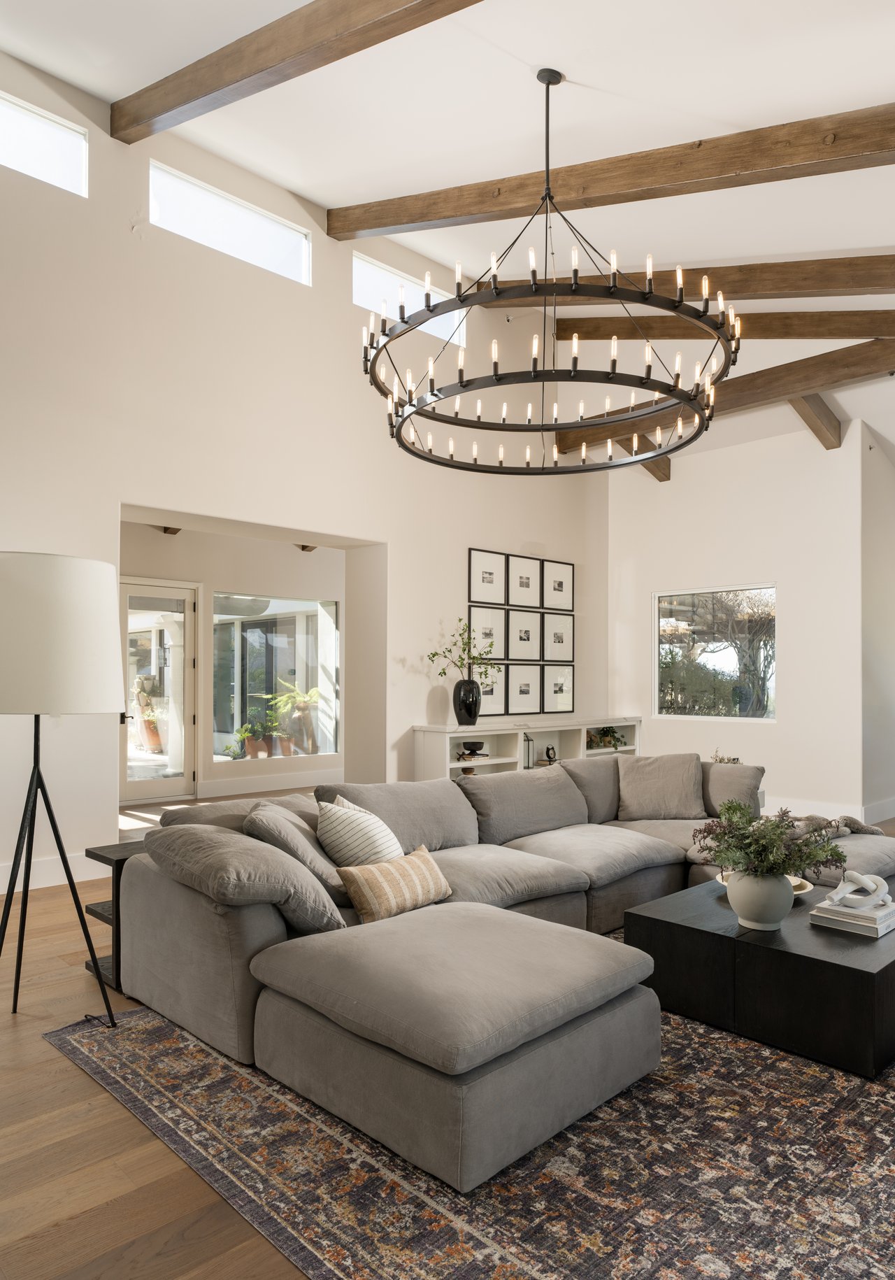 Living room with a gray sectional beneath exposed beams and a large circular chandelier.