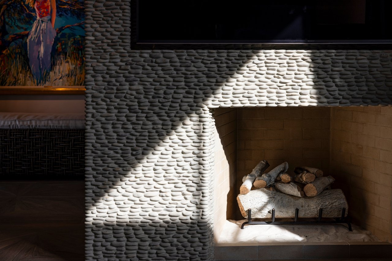 Living room fireplace with rounded gray stone surround, stacked logs, and television above.