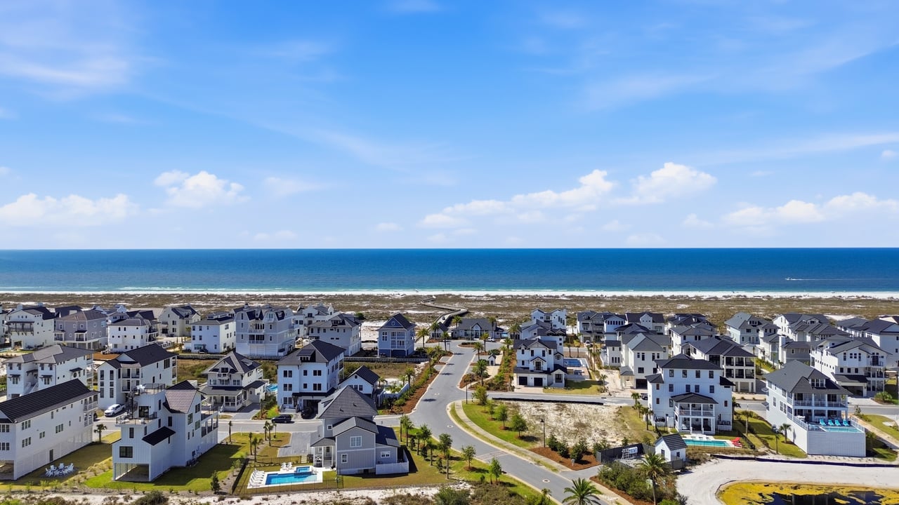 Aerial view of a coastal neighborhood with beachside homes, winding streets, and ocean beyond.