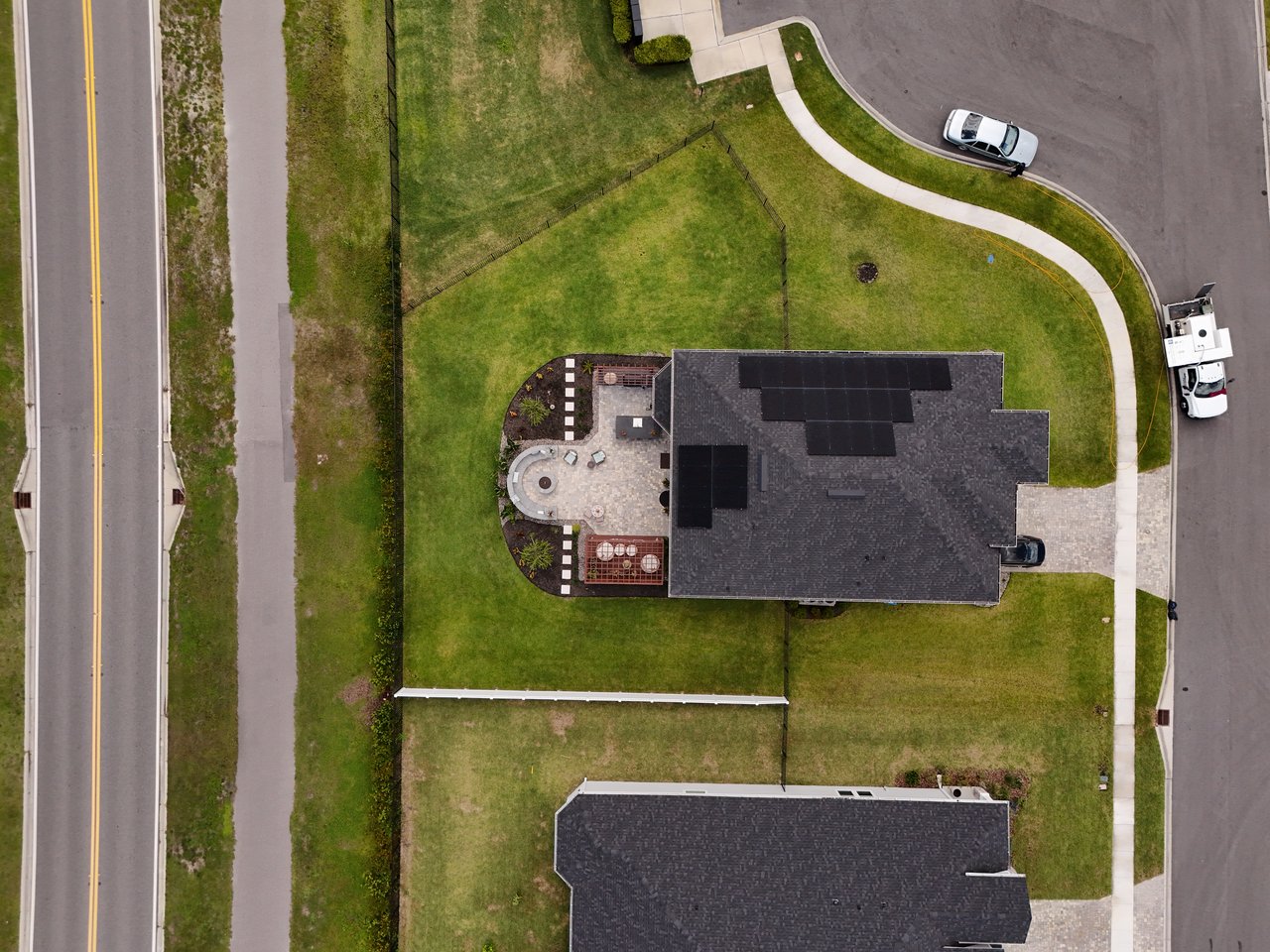 Aerial view of a home with rooftop solar panels and a paved backyard patio.