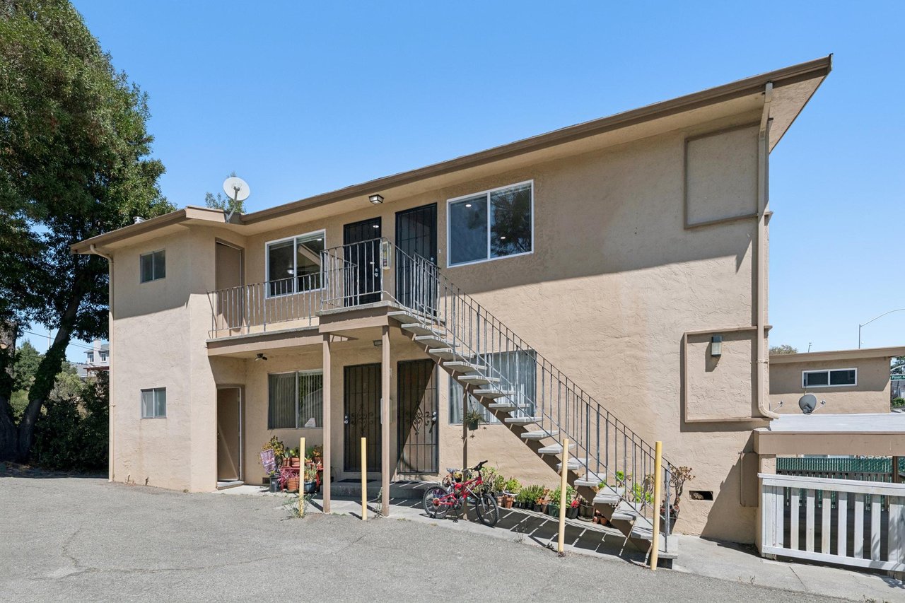 Beige stucco residence with an exterior metal staircase, upper-level balcony, and bicycles by the ground-floor entrance.