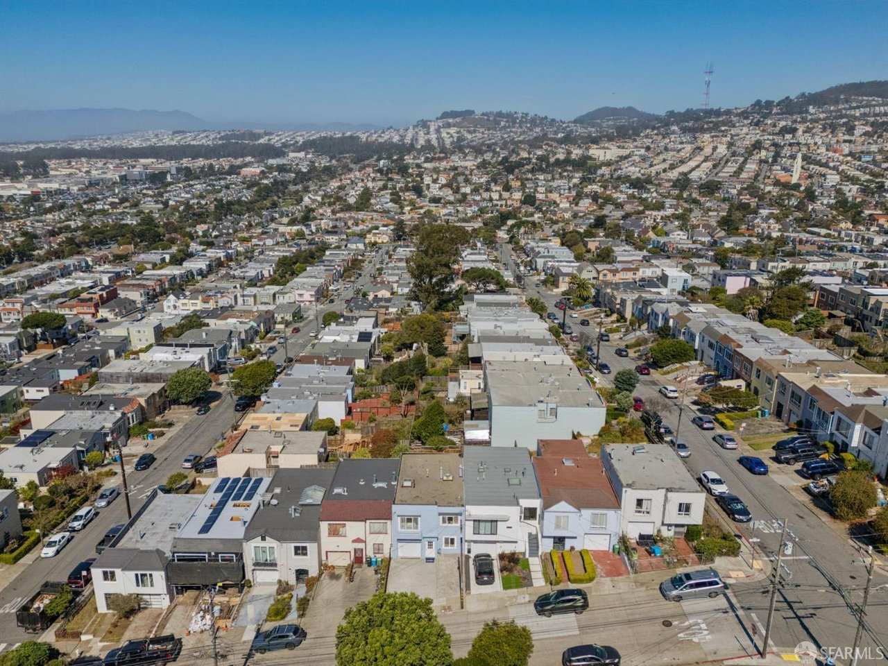 Aerial view over a dense neighborhood of homes, with San Francisco’s hills in the distance.