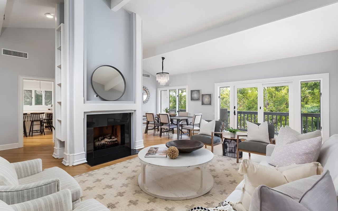 A bright, modern living room with a fireplace, a circular coffee table, and an adjacent dining area.