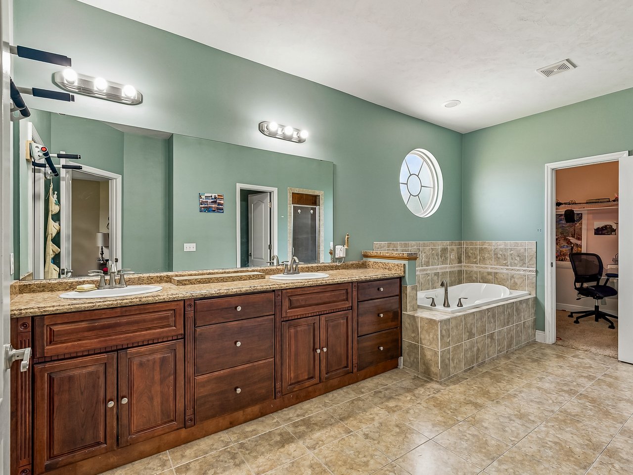Spacious bathroom with a dark wood double vanity, tiled soaking tub, and round window.