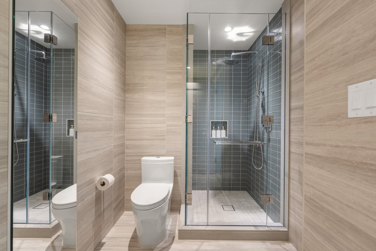 Modern bathroom with a glass-enclosed gray-tiled walk-in shower and beige stone-look walls.