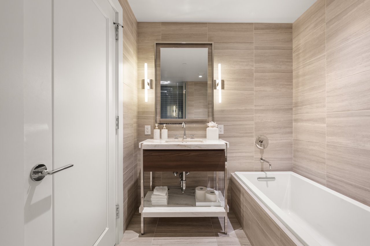 Bathroom with a soaking tub and dark wood vanity against beige tiled walls.
