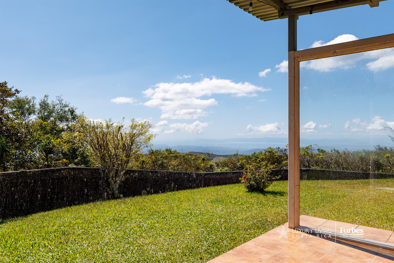Covered patio overlooking a grassy garden, distant mountain ridges, and blue water.