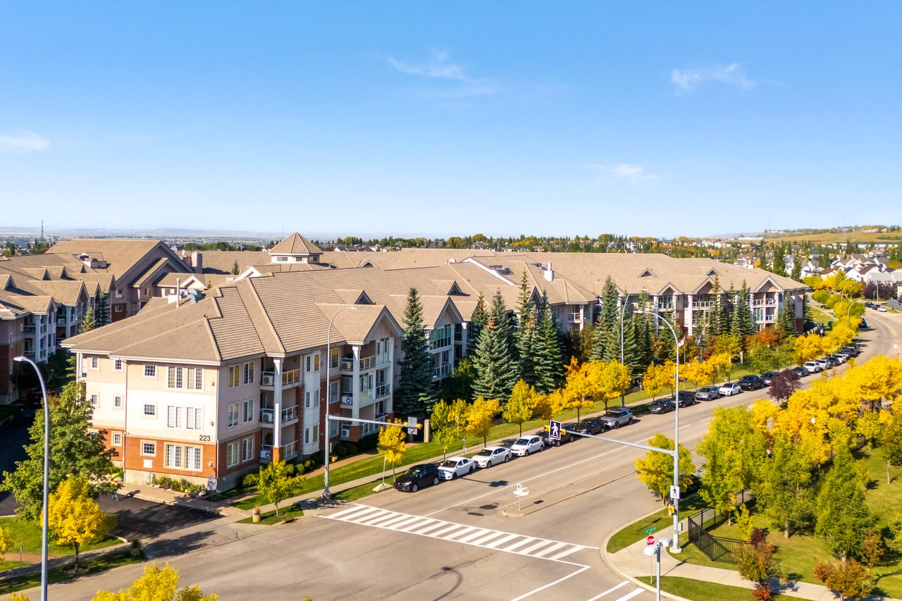 Condominium complex beside a tree-lined street and crosswalk, viewed from above.