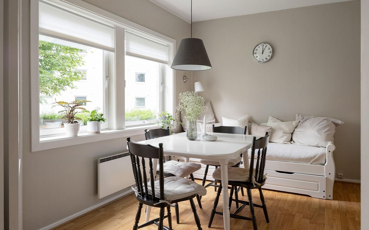 Dining area with a white table, dark chairs, built-in bench, and large windows.