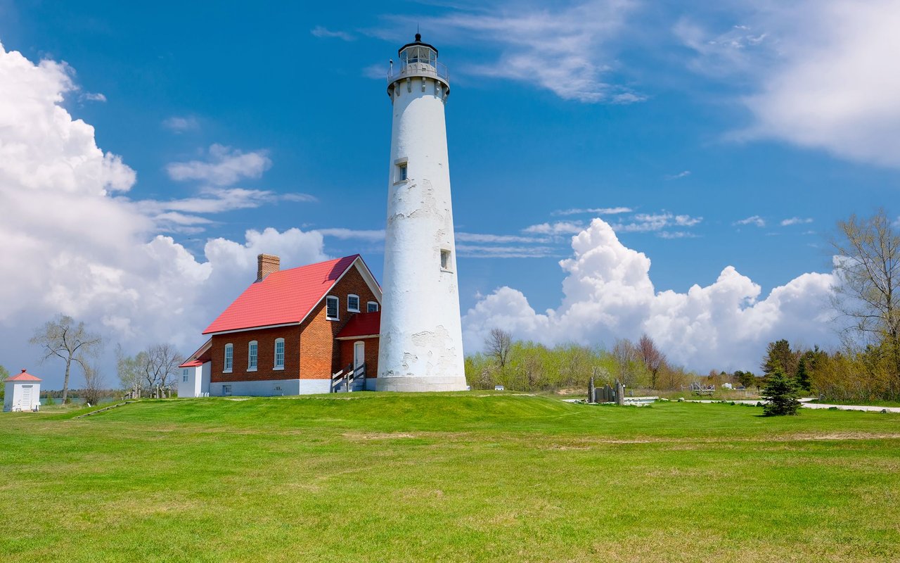 Fort Gratiot Lighthouse and its red-roofed brick keeper’s house on a green lawn.