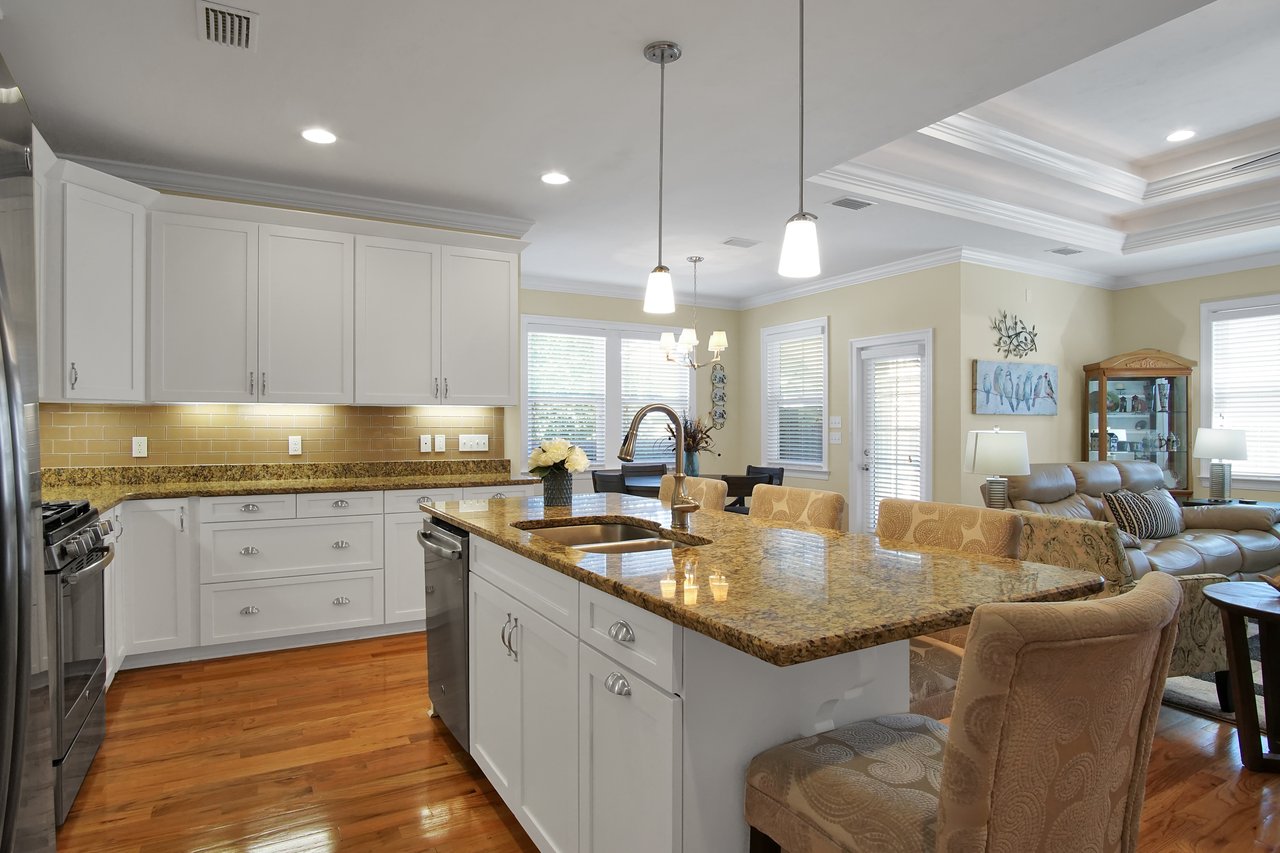 Bright kitchen and living area featuring white cabinetry, granite countertops, pendant lighting, and plush seating. Warm, inviting ambiance.