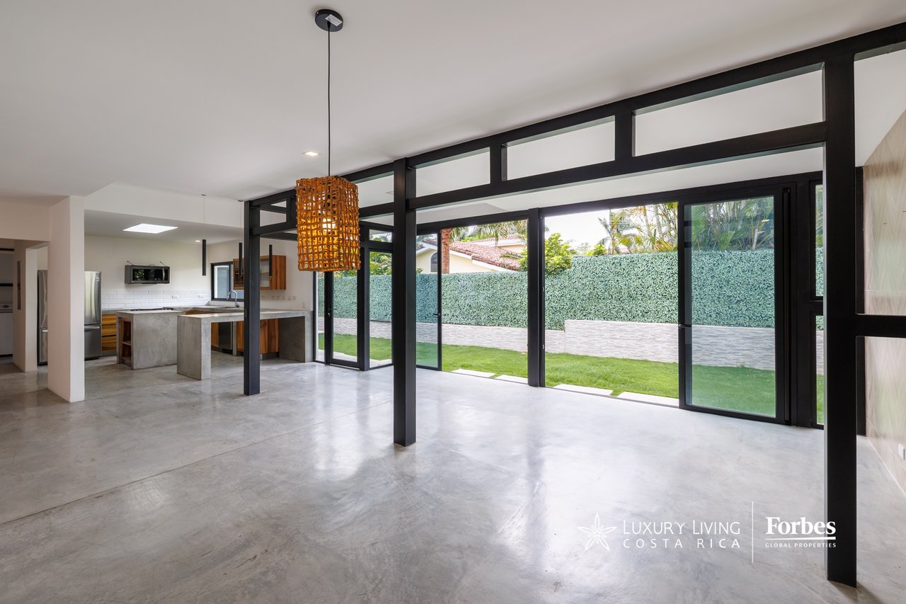 Open-plan kitchen and living area with polished concrete floors and black-framed glass doors opening to a garden.