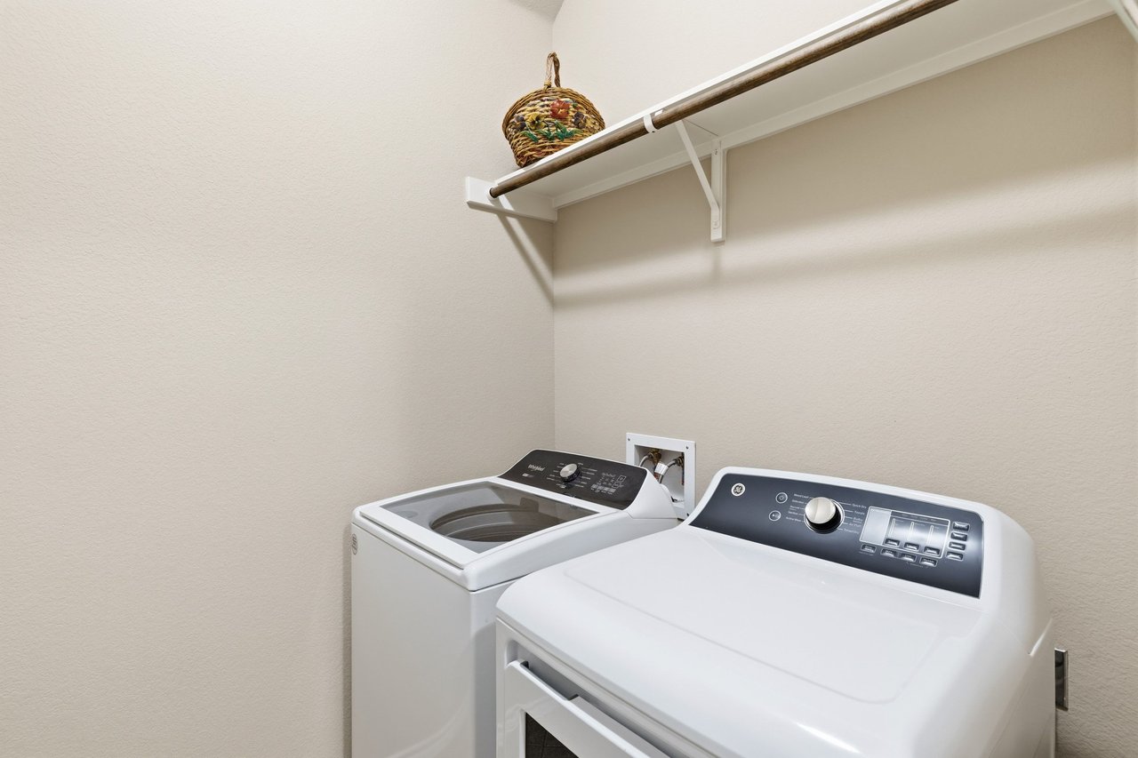 Laundry room with a white washer and dryer and an overhead shelf holding a woven basket.