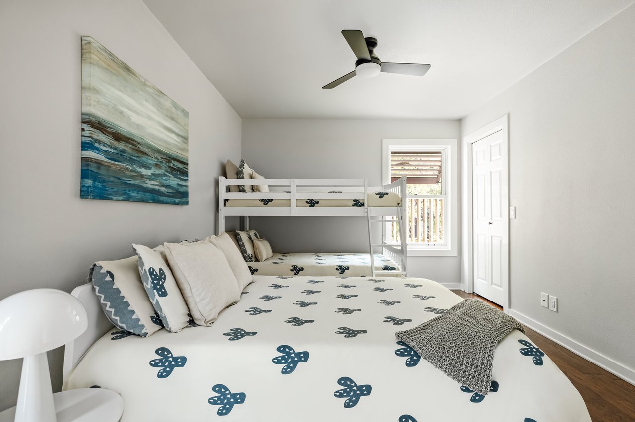 Furnished bedroom with blue-patterned bedding, a white bunk bed, and a window beside the beds.