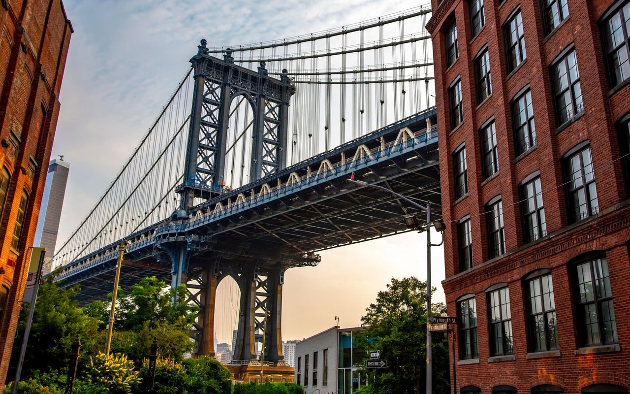 The Manhattan Bridge rises above a Dumbo street framed by red-brick buildings.