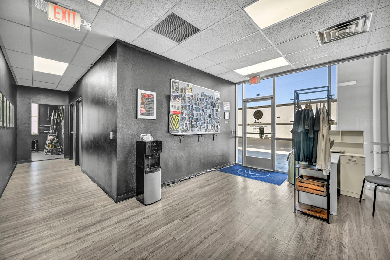 Commercial lobby with a glass entrance, coat rack, bulletin board, and hallway leading to a fitness area.