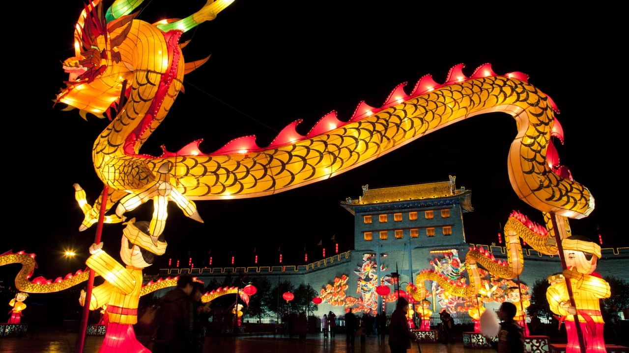 A glowing golden dragon lantern arches over a festival crowd and ornate gate at night.
